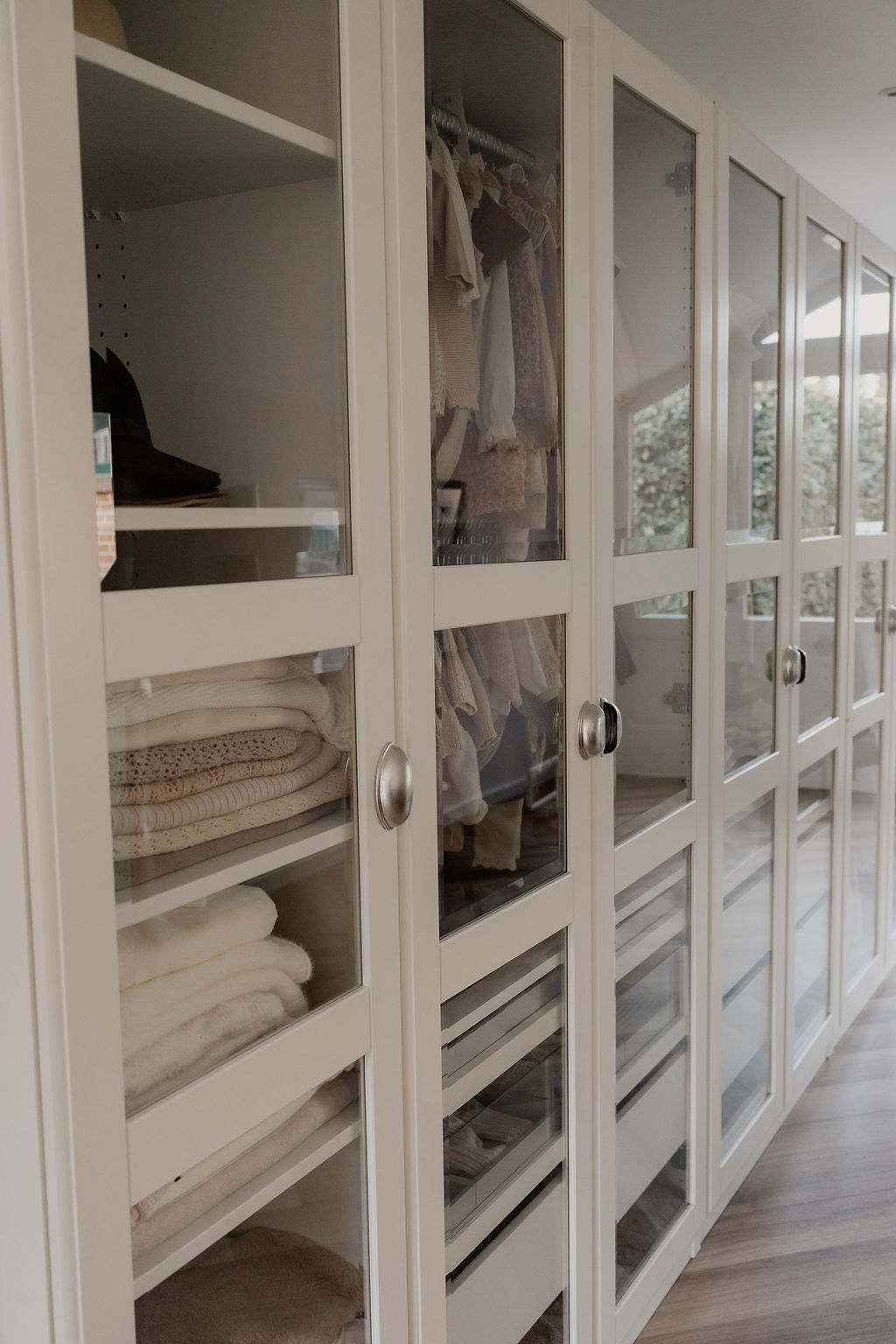 Landloft Studio - Weiße Glasschrankfronten mit gefalteten Stoffen und Kleidung